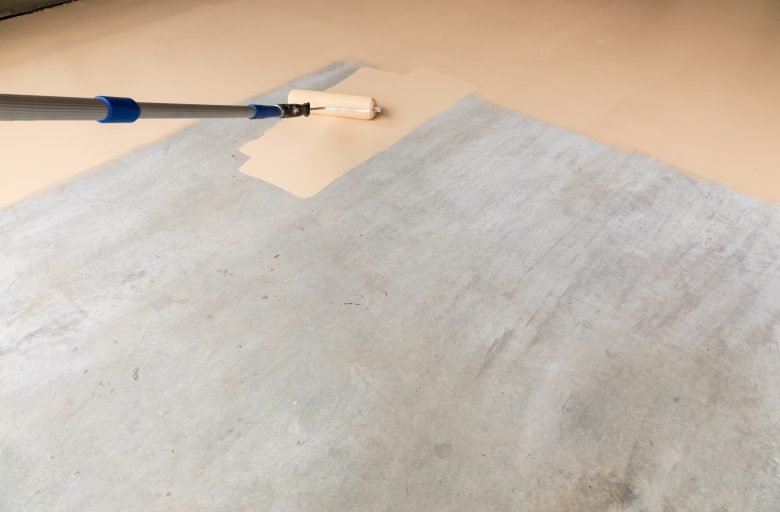 Worker Painting Floor of Garage with Roller.